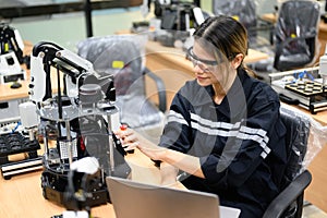 Female technician engineer using laptop checking automatic robotic machine