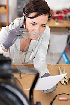 female technician making call on smartphone in workshop