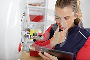 female technician servicing boiler using tablet computer