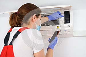 Female technician using smartphone and repairing air conditioner