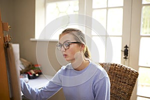 Female Teenage Artist Sitting At Easel Drawing Picture