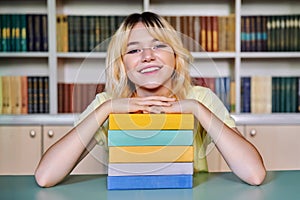 Female teenage high school student looking at camera with books in library