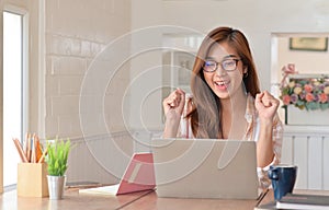 Female teenage students raise happy hands while studying online at home with a laptop