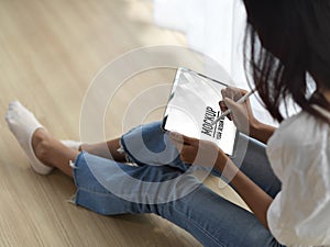 Female teenager using digital tablet on her knee while siting on the floor in living room