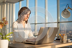 Female teleworker texting using laptop and internet, working online. Freelancer typing at home office, workplace. photo