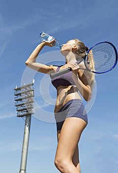 Female tennis player holds racket and drinking water