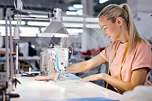 female textile factory worker on production line using modern sewing machine, at workshop