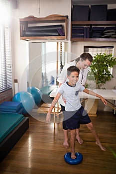 Female therapist holding boy standing on blue stress ball