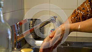 A female thoroughly washes her hands at a kitchen sink.
