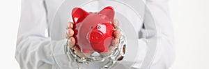 Female tied hands with chain hold red pig piggy bank closeup