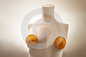 Female torso from a mannequin. Conceptual art. A minimalist female bust with orange slices on the nipples. Product advertisement