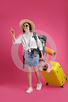 Female tourist with backpack, suitcase and travel pillow on pink background