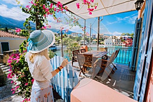 Female tourist with blue hat staying in Assos village in front of cozy veranda and admiring turquoise colored bay of