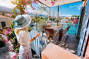 Female tourist with blue sun hat staying in Assos village in front of cozy veranda and enjoying turquoise colored bay of
