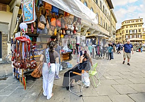 A woman shops for souvenirs from a small shop stand selling leather goods and clothing in Piazza Santa Croce in Florence Italy