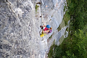 Female tourist, in colorful sport clothes, climbs a difficult vertical section on a via ferrata route above Hallstatt, Austria