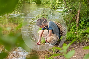 female tourist drinking clear water from calm river in forest during summer adventure