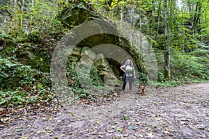 Female tourist hiker with her brown dachshund on a path taking a break next to a huge moss covered sandstone rock