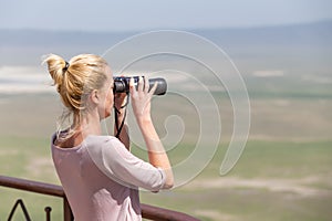 Female tourist looking through binoculars on African safari in Ngorongoro crater consrvation area, Tanzania, Afrika.