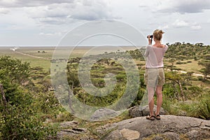 Female tourist looking through binoculars on African safari in Serengeti national park. Tanzania, Afrika. photo