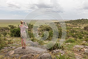 Female tourist looking through binoculars on African safari in Serengeti national park. Tanzania, Afrika.