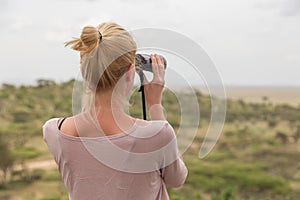 Female tourist looking through binoculars on African safari in Serengeti national park. Tanzania, Afrika.