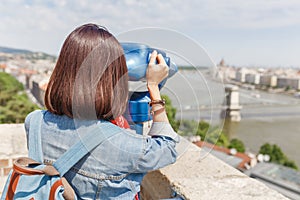 Female tourist looking through city telescope on the old town of Budapest. Travel and view point concept