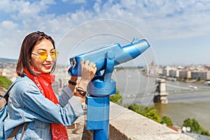 Female tourist looking through city telescope on the old town of Budapest. Travel and view point concept