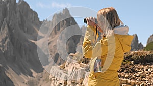 Female tourist looks through binoculars admiring mountains