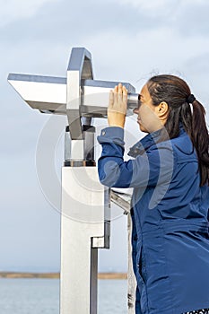 A female tourist looks through a binoscope on the observation deck. Concept: viewing stationary binoculars for tourists, coin bino