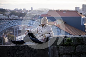 A female tourist poses on a stone wall near the Dom Luis Bridge in Porto, Portugal.