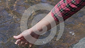 Female tourist`s hand touching the water surface at a river in the forest.