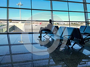 A female tourist, sitting on a chair in the departure zone of Ankara airport, looks out of the panoramic window at the plane. The