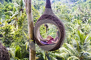 A female tourist is sitting on a large bird nest on a tree at Bali island