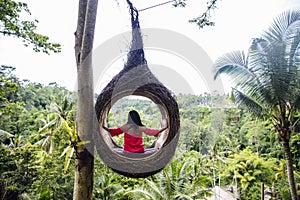 A female tourist is sitting on a large bird nest on a tree at Bali island