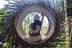 A female tourist is sitting on a large bird nest on a tree at Bali island
