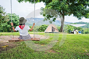 Female tourist sitting on swing, tent on green grass under trees.Holiday camping, beautiful view of the sky and mountains
