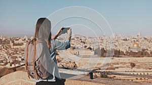 Female tourist takes photos of Jerusalem old town. Pretty Caucasian traveler woman smiling with backpack. Israel. 4K.