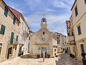 Female tourist taking photo of mall church on square of small urban village of Stari grad on Hvar island in Croatia