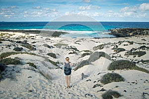 Female tourist visiting white beach of Caleta del Mojon Blanco. Sandy desert beach and rugged coastline. Orzola