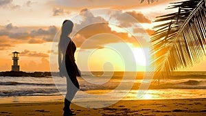 Female tourist walking barefoot along sea water waves on sandy beach. Young woman walks at seaside in romantic golden