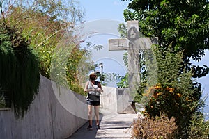 A female tourist wearing a facemask is walking towards the viewer. A cross from San CristÃ³bal Hill, Santiago is visible in the