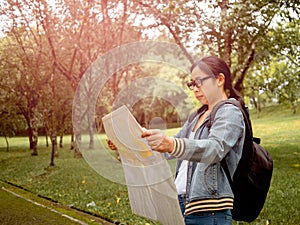 A female tourists with backpack relaxing outdoor and searching right direction on map in the forest. Freedom and lifestyle