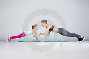 Female trainer and 10 years old girl are doing gym exercises