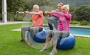 Female trainer assisting active senior couple to exercise with dumbbells