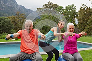 Female trainer assisting active senior couple to exercise with dumbbells
