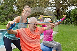 Female trainer assisting active senior couple to exercise with resistance band