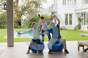 Female trainer assisting active senior couple to exercise with resistance band in the porch