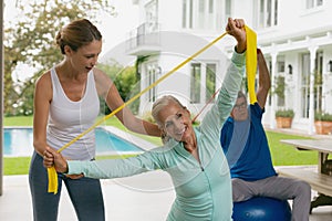 Female trainer assisting active senior couple to exercise with resistance band in the porch