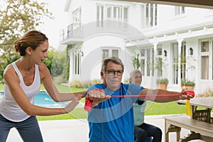 Female trainer assisting active senior couple to exercise with resistance band in the porch